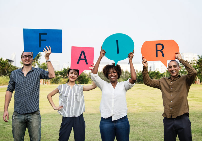 Diverse group of people standing outside on a field holding the letters F A I R